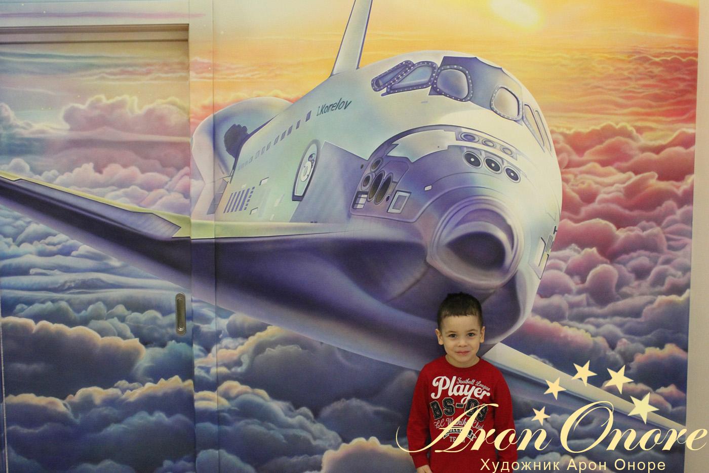 Счастливый мальчик на фоне художественной росписи стены в детской