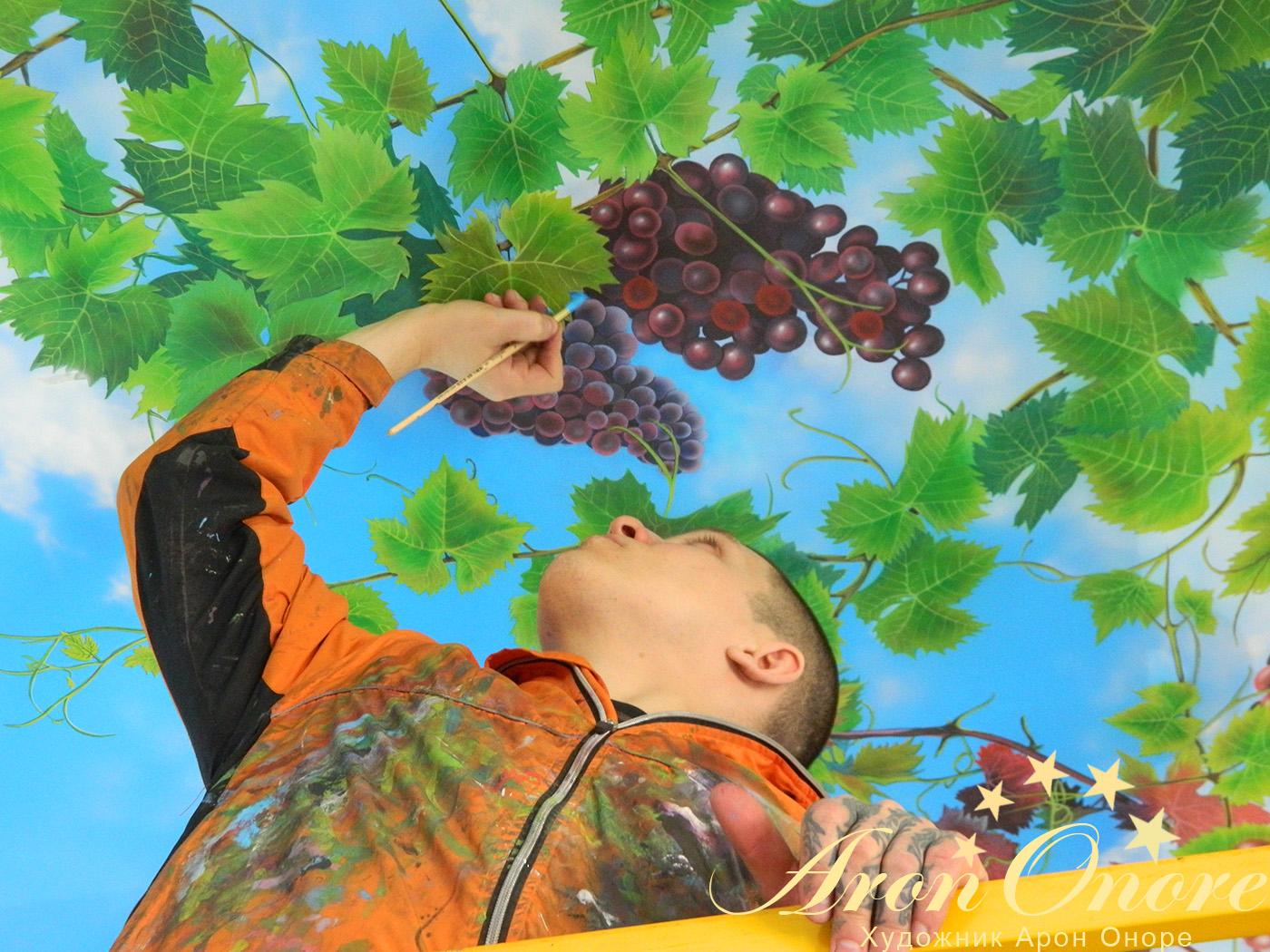 Художник аэрограф создает рисунок на потолке – виноградная лоза на фоне синего неба